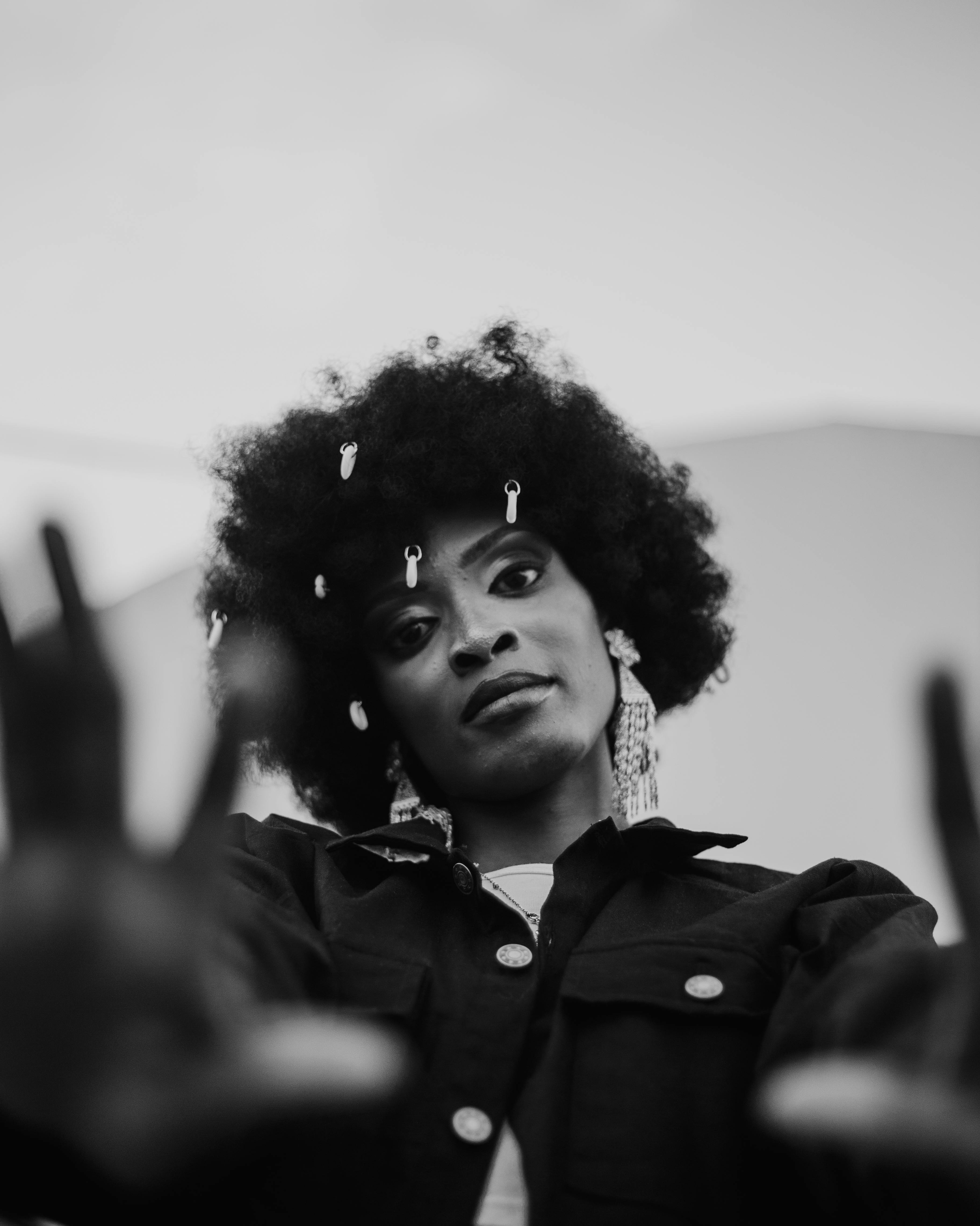 A woman with an afro wearing a jacket and holding her hands up